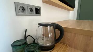 Uma área de cozinha com bancada de madeira, uma cafeteira de vidro e três potes de vidro verdes.