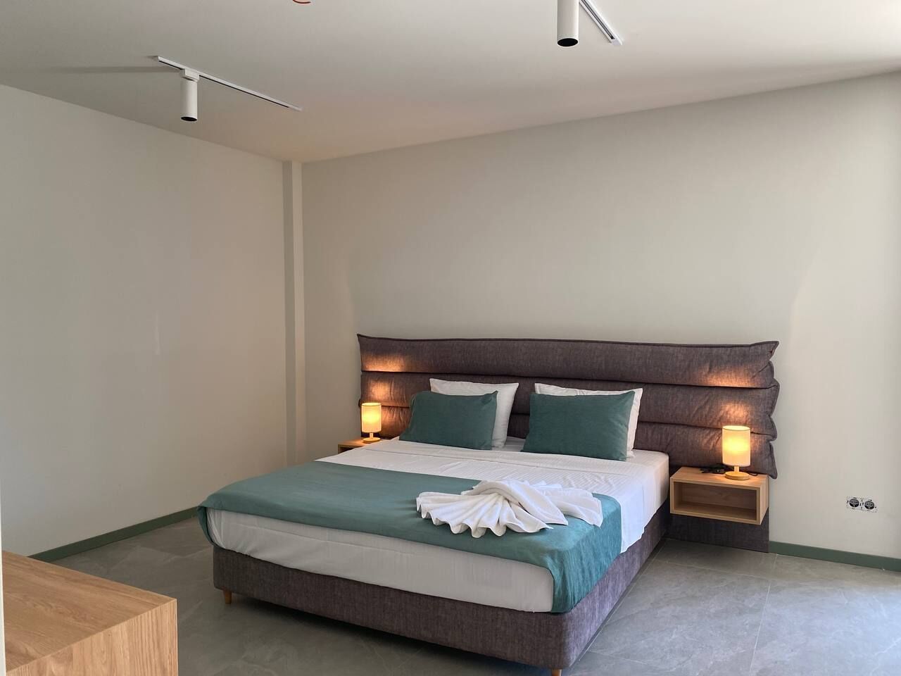 Una cama bien hecha con un cabecero, dos mesitas de noche con lámparas y un pequeño mueble de madera.