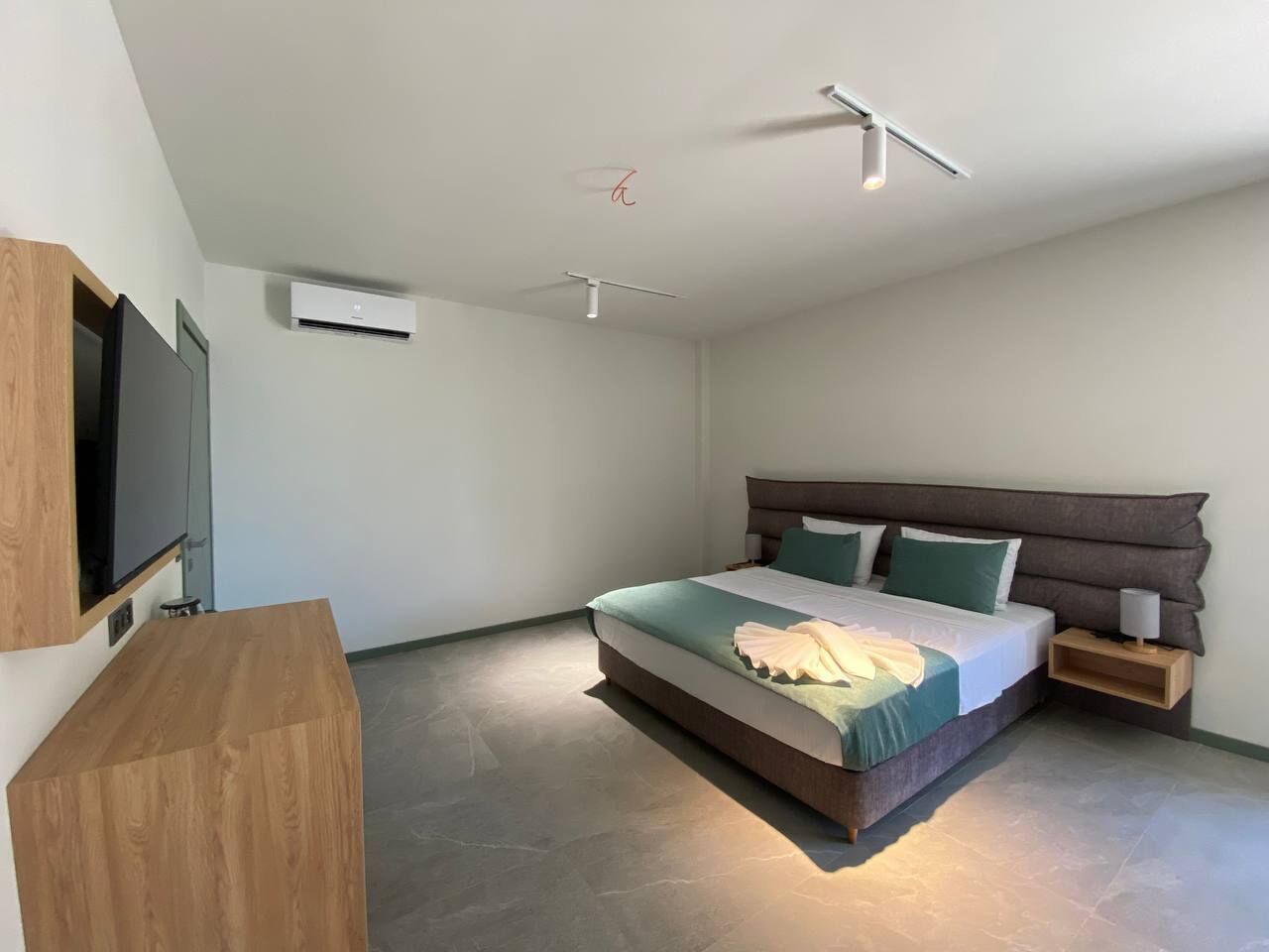 Un dormitorio moderno con una cama grande, un televisor montado en la pared y un escritorio de madera.