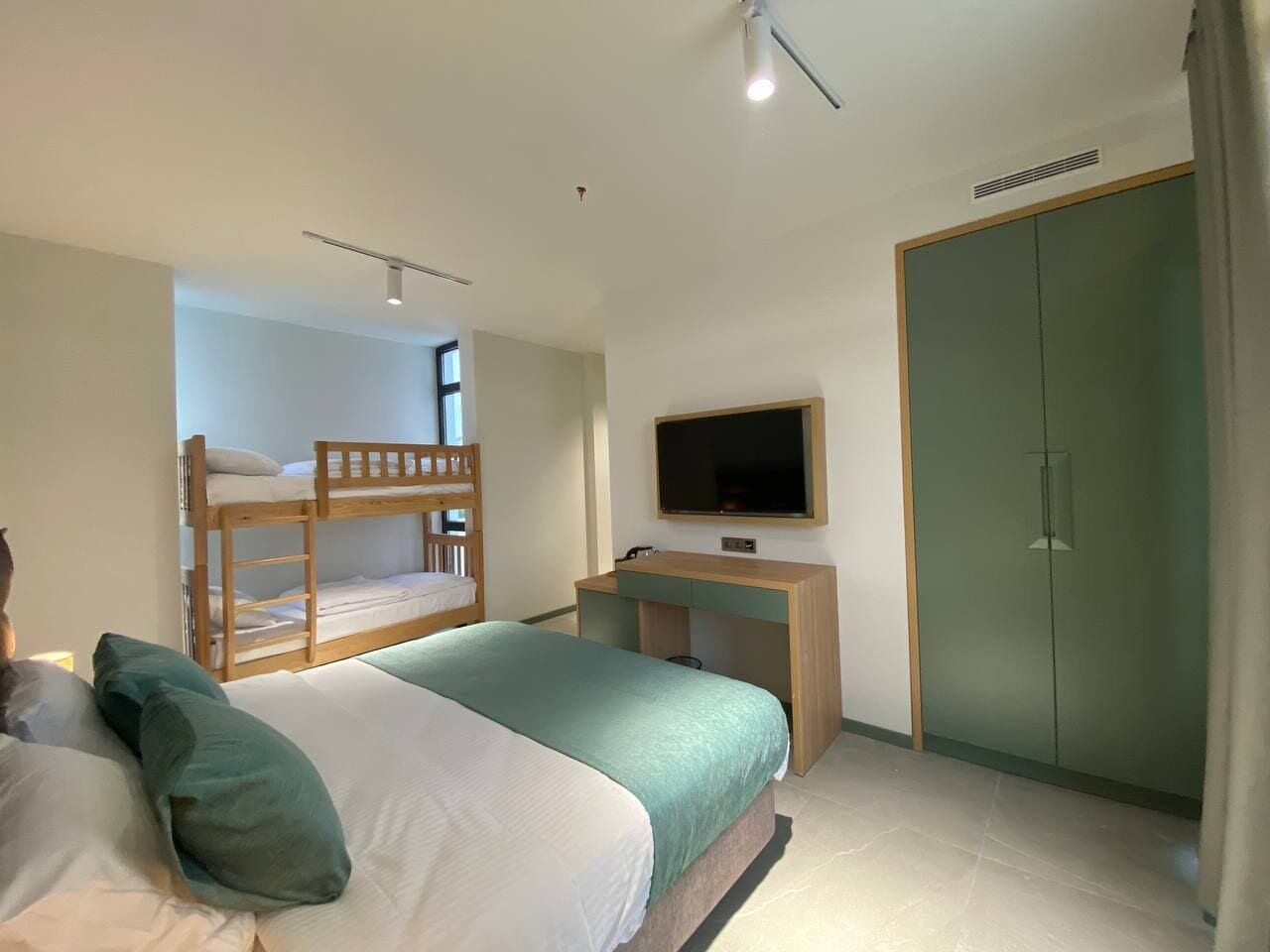 A bedroom with a bunk bed, a desk, a television, and a wardrobe.