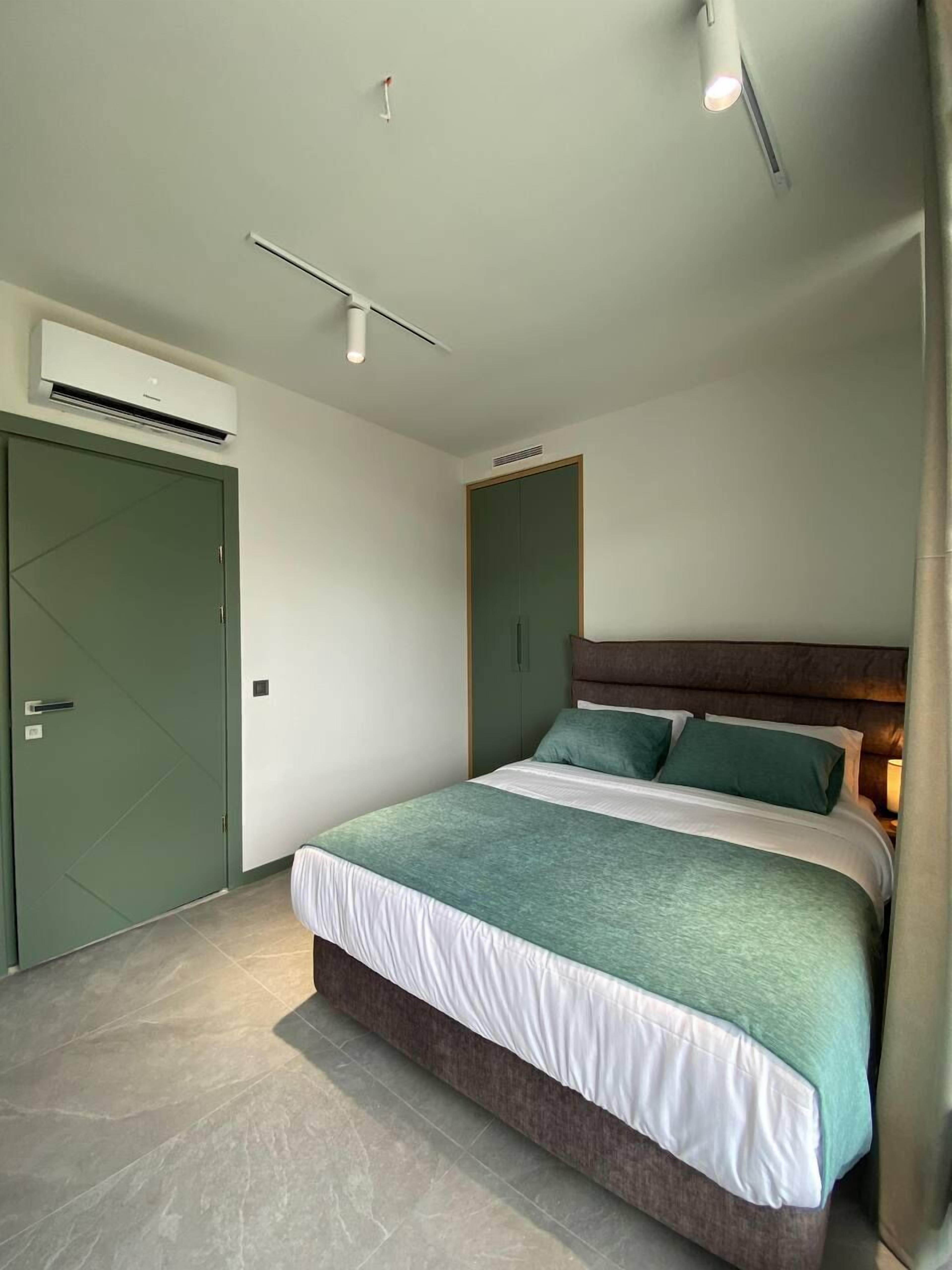 A modern bedroom with a bed, green and white bedding, a wooden headboard, and a green wardrobe.