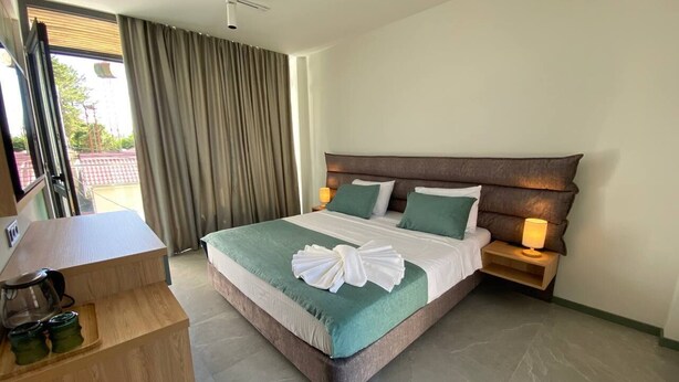 A hotel room with a large bed, a wooden desk, a nightstand with a lamp, and a view of the outside through a window with curtains. - H2O Ureki (Ureki)