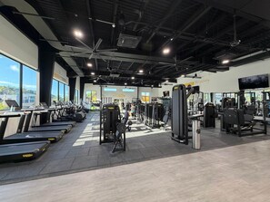 Une salle de sport équipée de tapis de course, d’appareils de musculation et dotée d’une grande fenêtre.