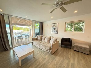 Un salon comprenant un canapé, une petite table, un fauteuil, un ventilateur de plafond et une fenêtre.