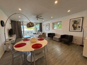 Un salon moderne avec une table de salle à manger ronde, des canapés, un ventilateur de plafond et de grandes fenêtres.