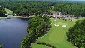 An aerial view of a golf course with a lake, surrounded by dense forest and residential buildings. - Beachside Luxury Villa, Balcony Views! Hilton Head (Hilton Head Island)