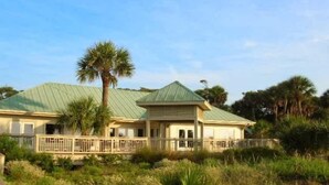A two-story building with a green roof, surrounded by palm trees and a wooden deck. - Beachside Luxury Villa, Balcony Views! Hilton Head (Hilton Head Island)