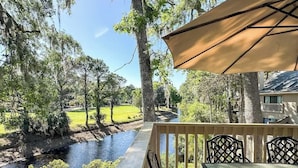 A deck with a table and chairs, overlooking a river and a golf course. - Beachside Luxury Villa, Balcony Views! Hilton Head (Hilton Head Island)