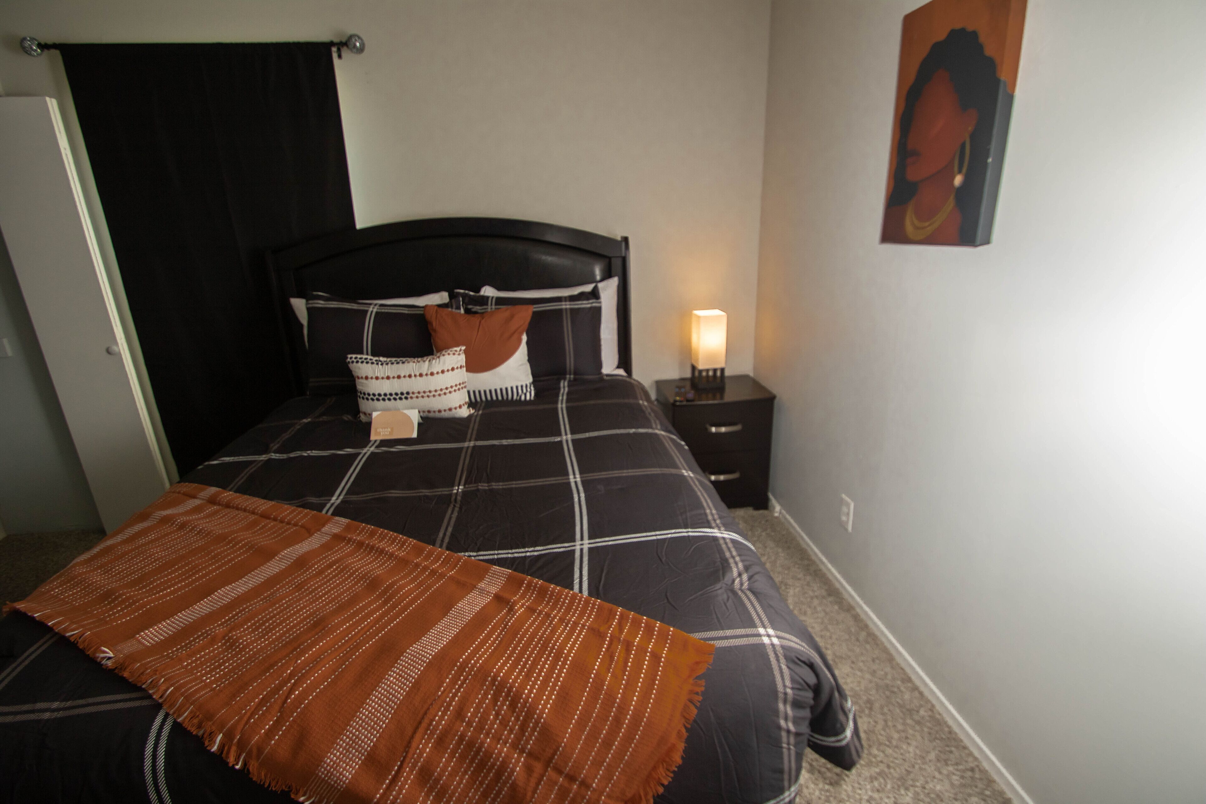 Un dormitorio con cama, mesita de noche, lámpara de pared y puerta.
