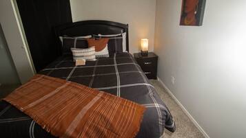 Un dormitorio con cama, mesita de noche, lámpara de pared y puerta.