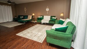 Un salon avec un mur marron, des canapés verts, un tapis blanc et deux lampes fixées au mur.