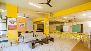 A spacious room with yellow walls, a large table, multiple chairs, a sofa, and a ceiling fan. - COVIE Bannerghatta 141 (Bengaluru)