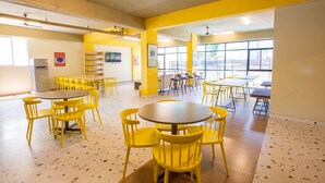 A spacious dining area with yellow chairs and tables, large windows, and a kitchenette. - COVIE Bannerghatta 141 (Bengaluru)