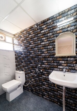 A bathroom with a stone-patterned wall, a toilet, a sink, and a mirror. - COVIE Bannerghatta 141 (Bengaluru)