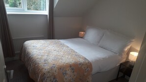 Un lit simple avec une couette à motifs floraux, une lampe de chevet et une fenêtre avec des rideaux.