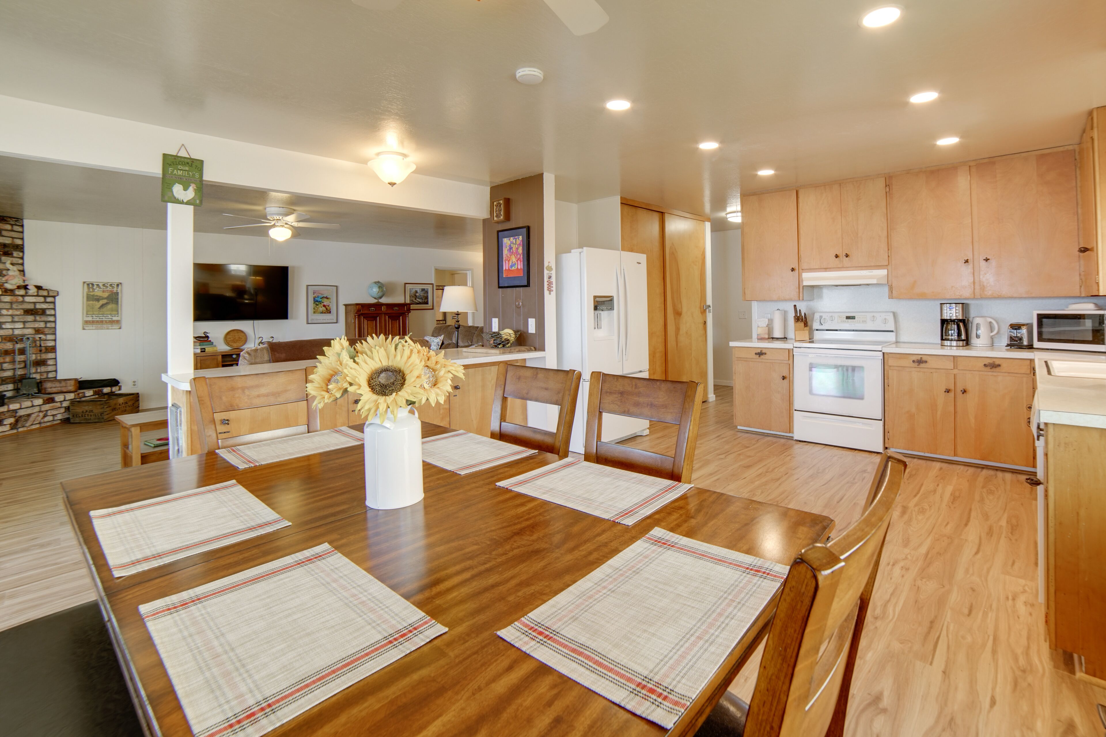 Una cocina amplia con armarios de madera, una mesa de comedor con individuales y un jarrón central con girasoles.