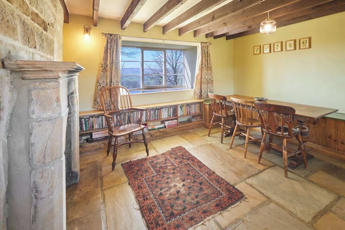 Un coin repas chaleureux avec une cheminée en pierre, des chaises en bois, une longue table et une bibliothèque remplie de livres.