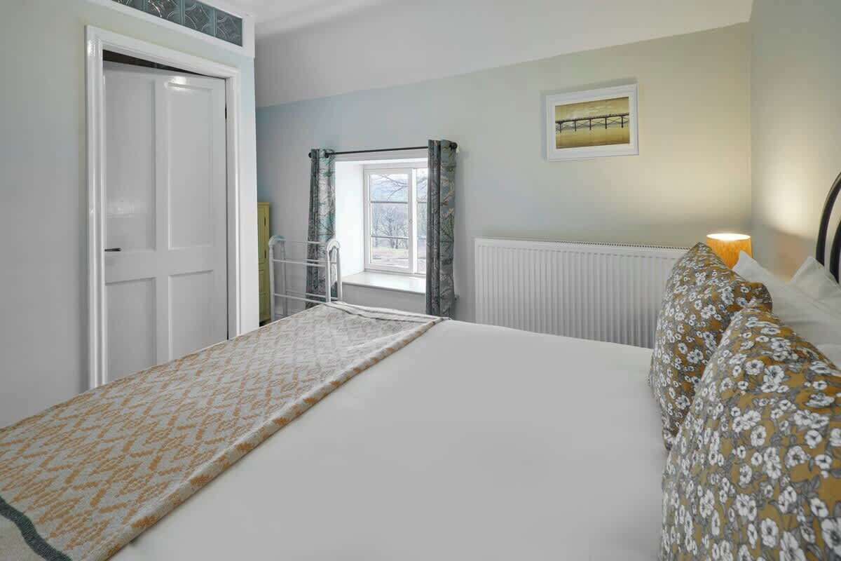 Een slaapkamer met een bed, een radiator, een raam met gordijnen en een deur.