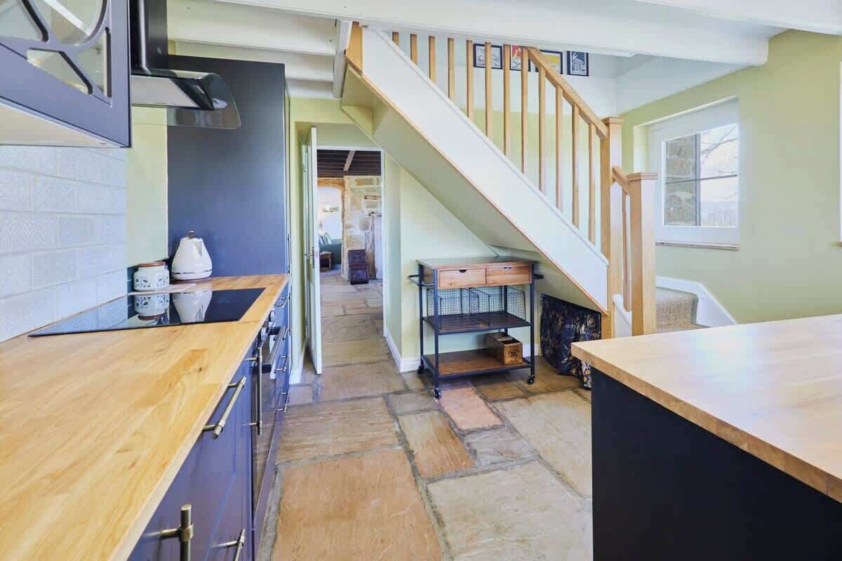 Una cocina con encimera de madera, una escalera y vistas al salón.