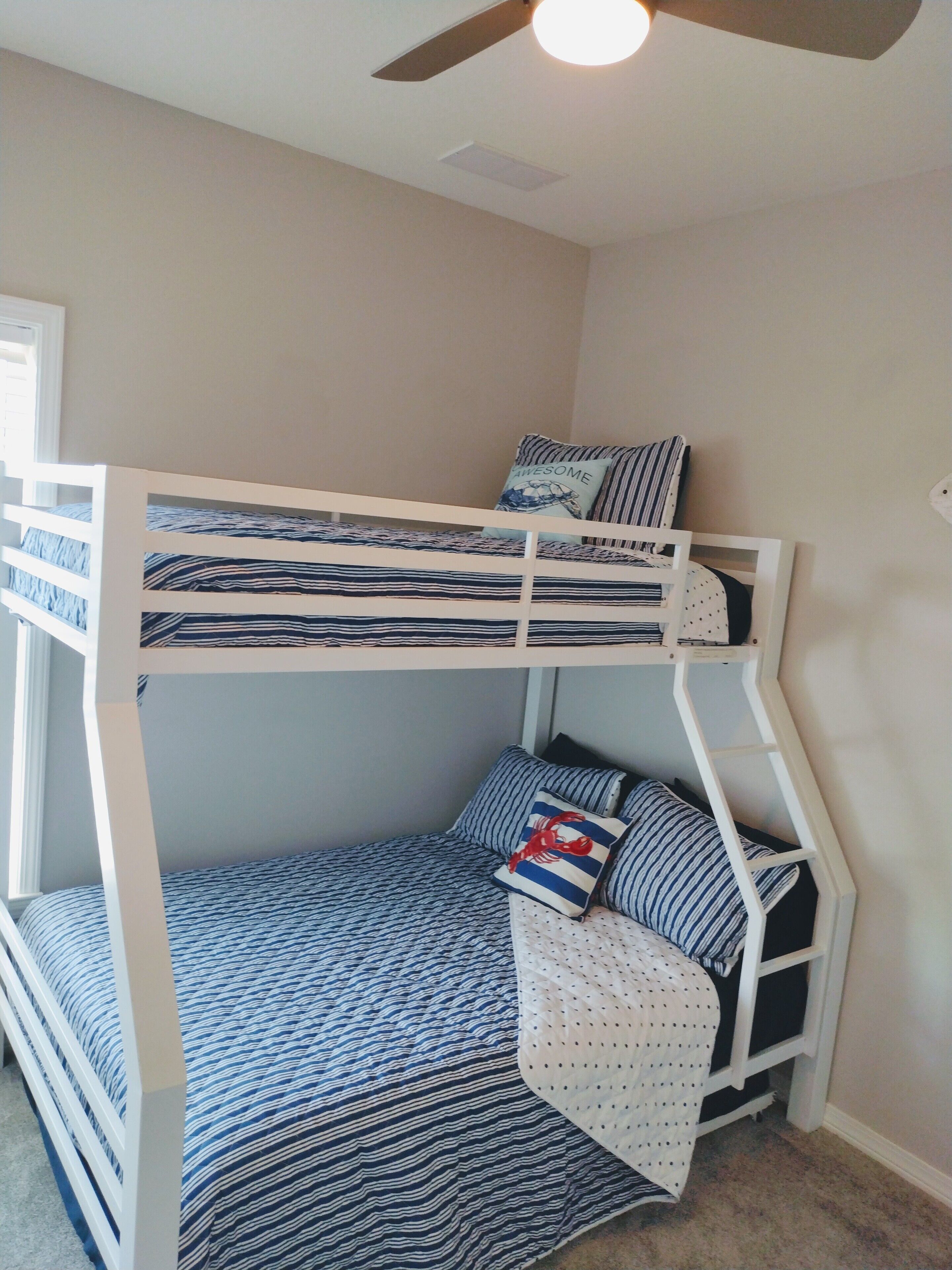 A bunk bed with striped bedding, a ceiling fan, and a window with blinds.