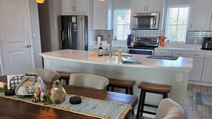 A modern kitchen with white cabinets, a central island, and pendant lighting. - Salty and Sweet at Perdido Key  SLEEPS 8! Two pools and a state-of-the-art gym (Pensacola)
