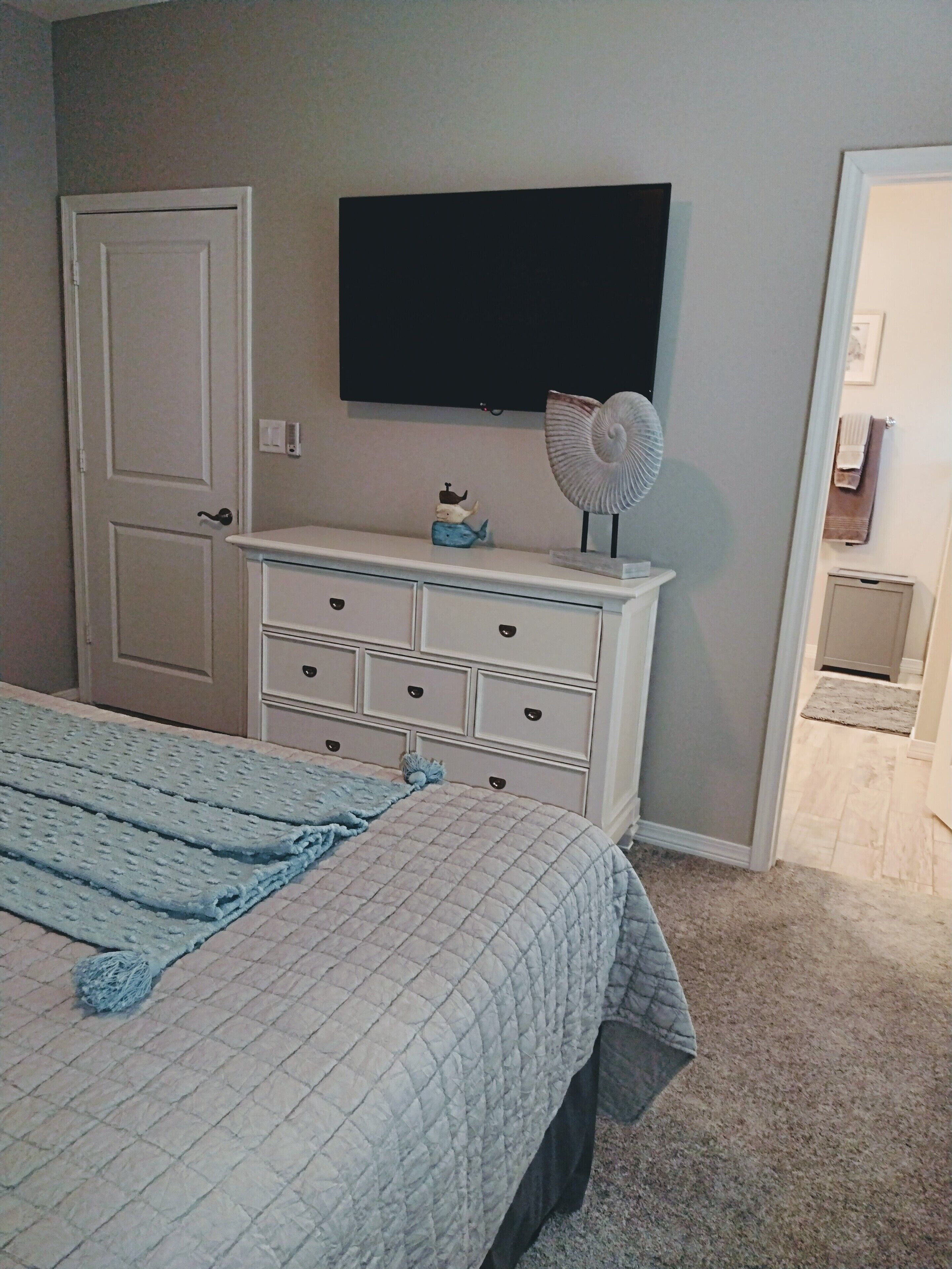 A bedroom with a bed, dresser, and a wall-mounted TV.