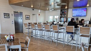 A restaurant with wooden flooring and metal chairs. There are tables with chairs, a counter with a TV, and a refrigerator in the background. - Salty and Sweet at Perdido Key  SLEEPS 8! Two pools and a state-of-the-art gym (Pensacola)