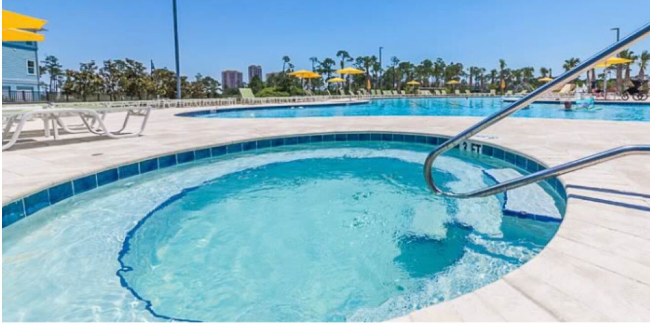 Una piscina con agua azul cristalina, rodeada de sillas de descanso y sombrillas, con palmeras y edificios al fondo.