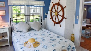 Een slaapkamer met een bed, een nachtkastje, een raam met gordijnen, een aan de muur bevestigd scheepsschroef en uitzicht op de omgeving.