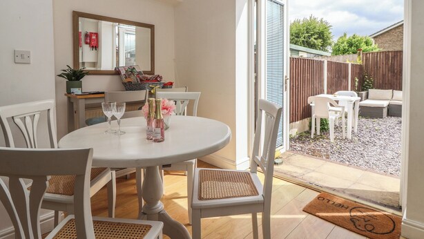 A dining area with a round table, white chairs, a mirror, and a view of the backyard.