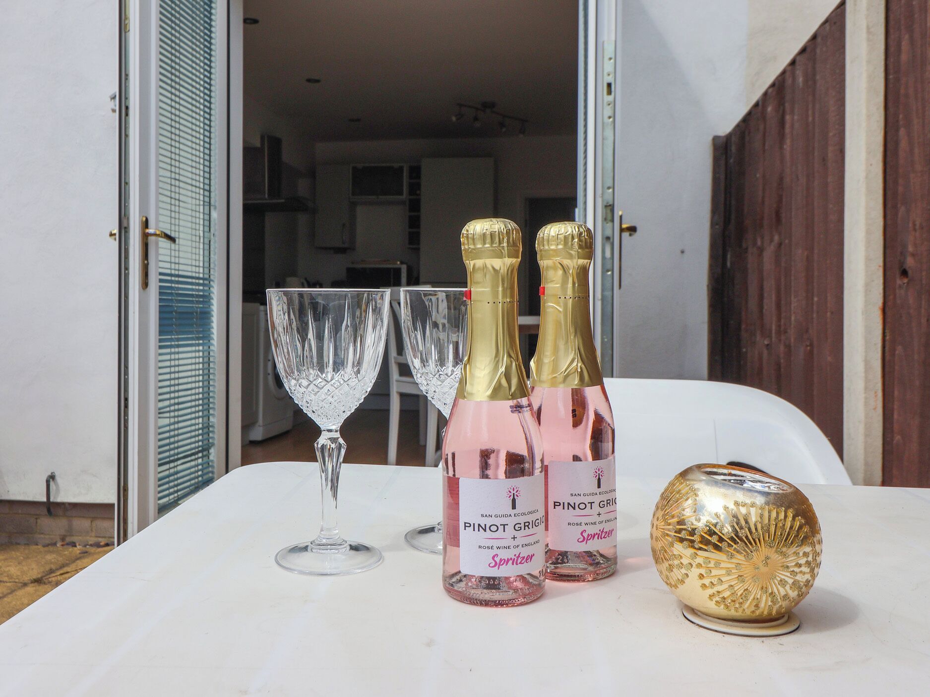 Uma mesa com duas garrafas de San Guida Ecologica Pinot Grigio, dois copos de vinho e uma esfera dourada decorativa.