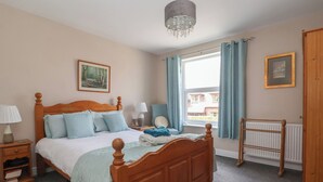 A bedroom with a wooden bed, a nightstand, a chair, a radiator, and a window with curtains.