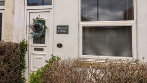 A white building with a door labeled 'Bluebell Cottage,' a window with blinds, and a number plate.