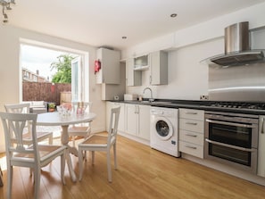 A modern kitchen with a washing machine, oven, and dining area with chairs and a table.