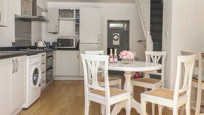 A compact kitchen with a washing machine, microwave, and a dining area with white chairs and a table.