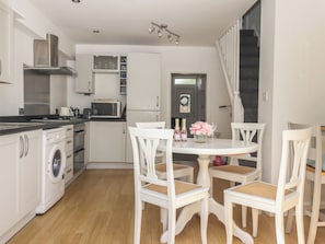A compact kitchen with a washing machine, microwave, and a dining area with white chairs and a table.