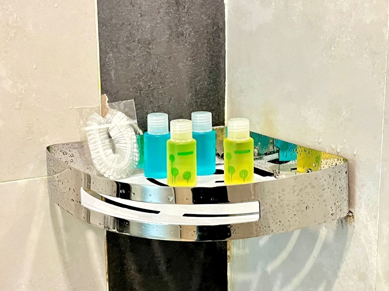 A bathroom with a chrome towel rack holding a white towel, a blue bottle, and three green bottles with tree designs.