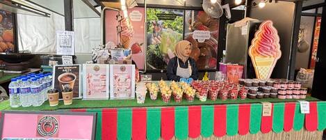 A food stall with a variety of drinks and desserts, including a large ice cream cone and multiple cups of chocolate and strawberry flavored beverages.