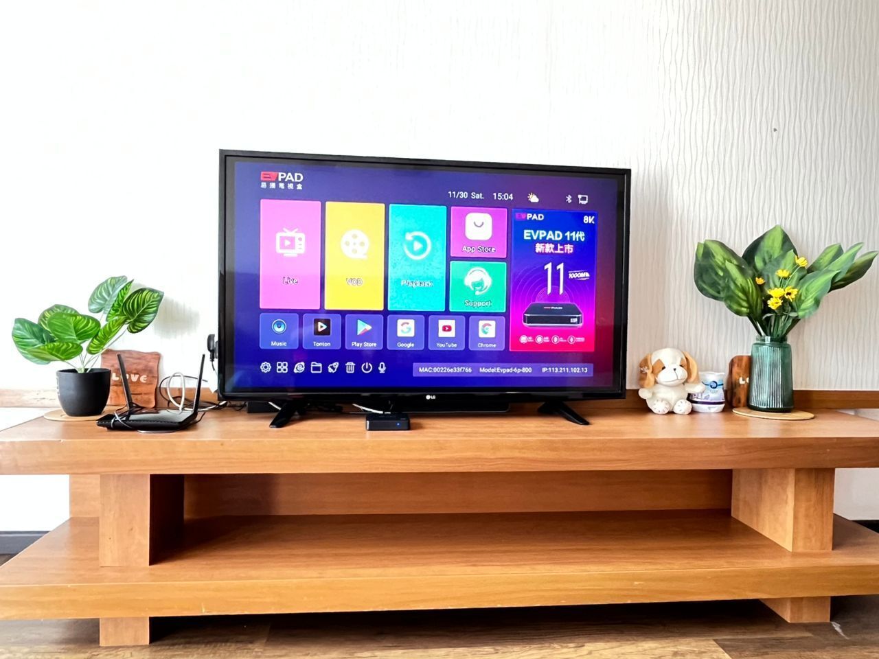 A flat-screen TV on a wooden stand with a colorful interface, a small figurine, and a potted plant.