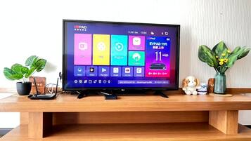 A flat-screen TV on a wooden stand with a colorful interface, a small figurine, and a potted plant.