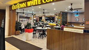 Interior de una cafetería con mesas, sillas y una barra.