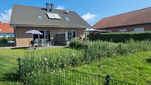Una casa con fachada de ladrillo, techo de tejas y patio trasero cercado con zona de barbacoa.
