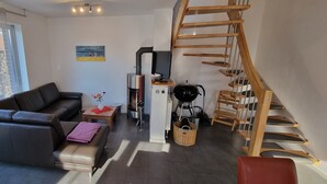 Una sala de estar moderna con un sofá de cuero, una pequeña mesa con un florero, una escalera de madera y vistas al exterior.