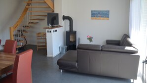 Una sala de estar moderna con una escalera de madera, un sofá, una mesa de comedor con sillas y una chimenea.