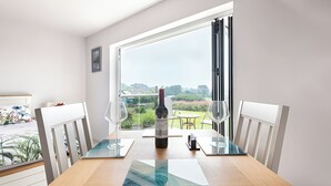A dining table with a bottle of wine, two wine glasses, and a placemat in a room with a large window overlooking a garden.