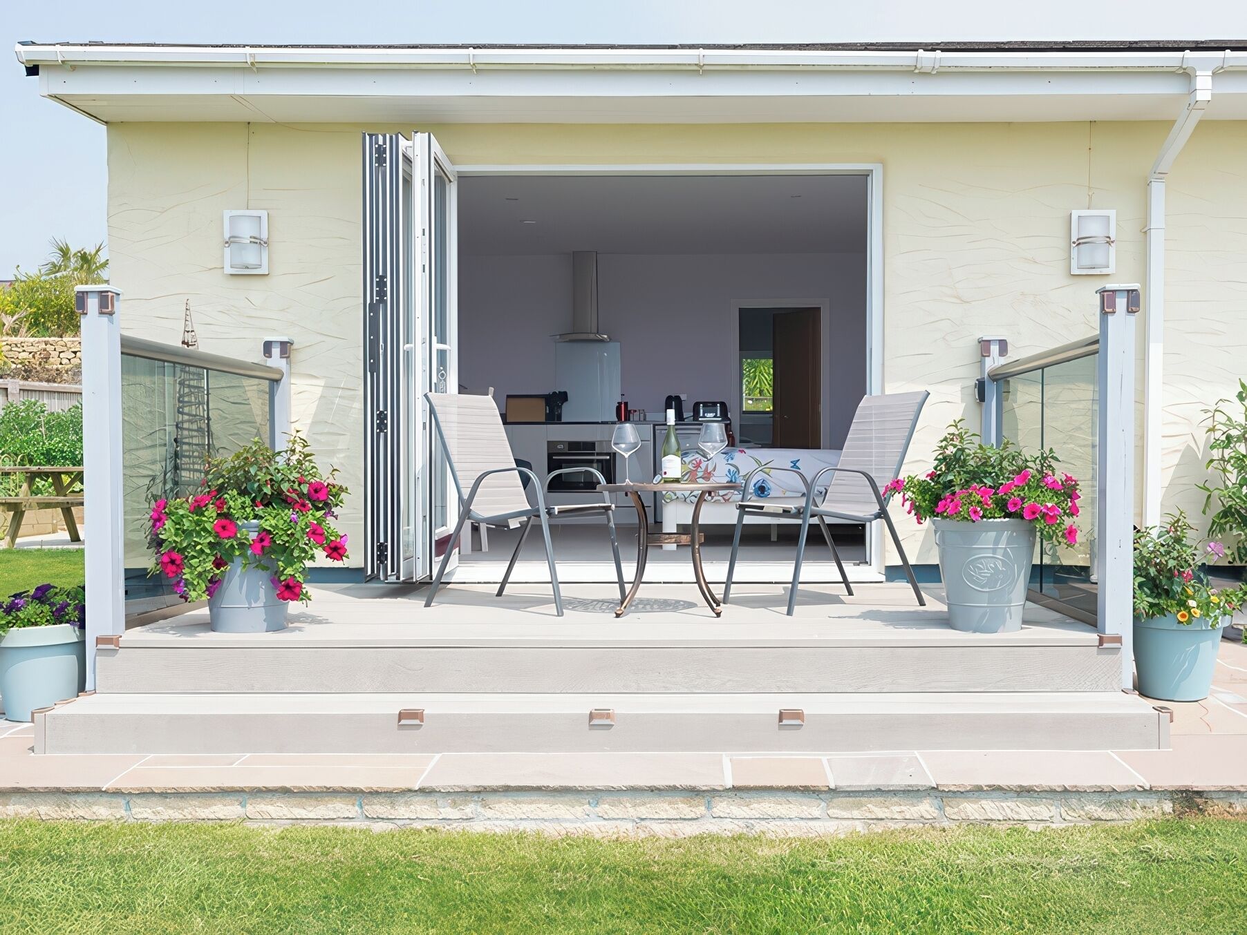 A modern outdoor patio with a dining table and chairs, a sliding glass door leading to a kitchen, and potted plants.