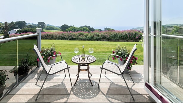 A balcony with two chairs and a table, overlooking a well-maintained garden and distant hills.