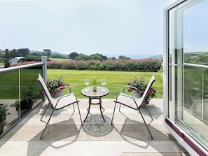 A balcony with two chairs and a table, overlooking a well-maintained garden and distant hills. - Greenside Studio (Penzance)