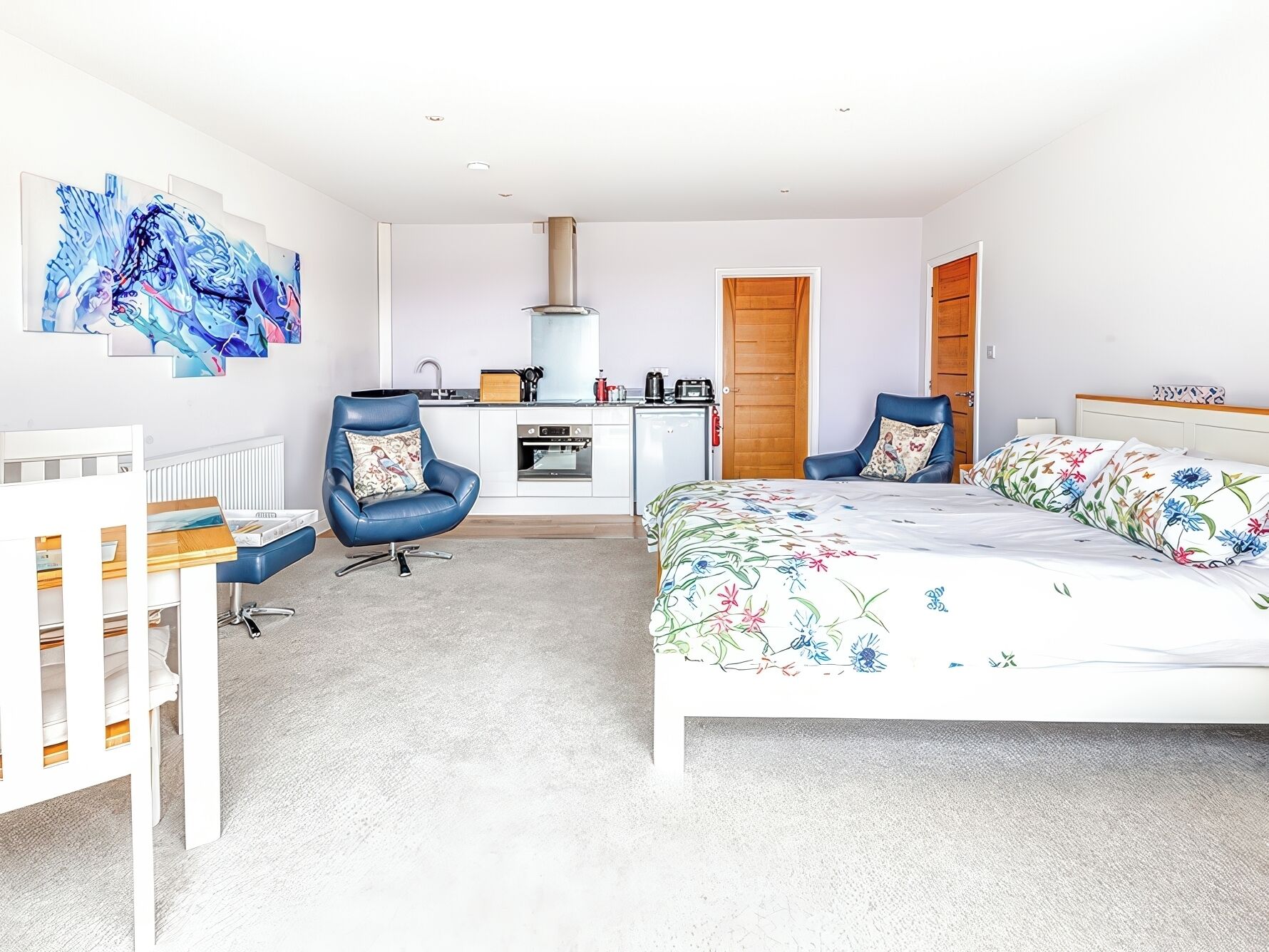 Un dormitorio moderno con cama, dos sillas, escritorio, radiador y una zona de cocina.