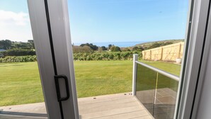 A balcony with a glass door leading to a grassy yard and a view of the sea.